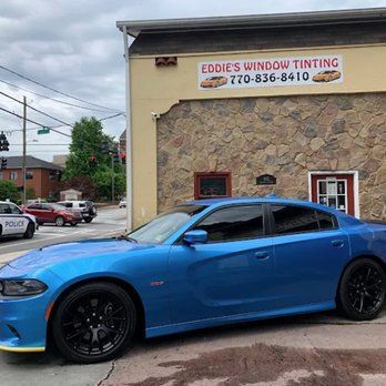 Blue sports sedan parked outside Eddie’s Window Tinting shop on a cloudy day