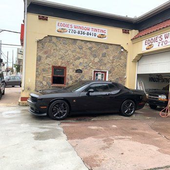 Black sports car parked outside Eddie’s Window Tinting shop on a wet street.