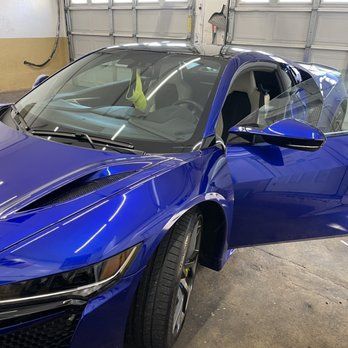 Blue sports car with front-end damage parked in a garage, driver’s door open