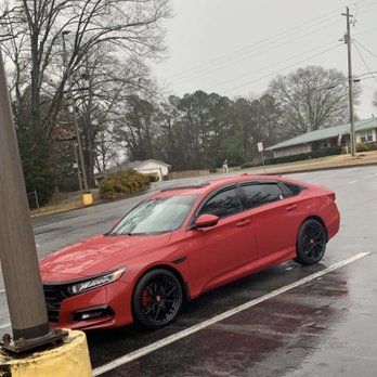 Red sports coupe parked in a wet lot beside a utility pole on an overcast day
