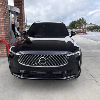 Black Volvo SUV parked at a gas station, front view near a brick building.