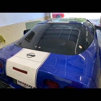 Blue sports car with white center stripe parked indoors, rear view