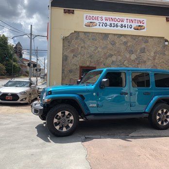 Blue Jeep parked outside Eddie’s Window Tinting shop with a tan car in the background