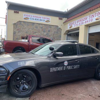 Black state police sedan parked outside Eddie's Window Tinting with a red pickup in the background