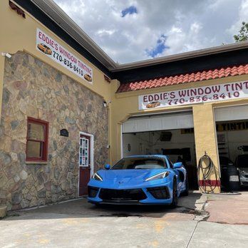 Blue sports car outside Eddie’s Window Tint shop under a stone-front building.