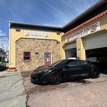 Black sports car parked outside a stone auto tinting shop with an open garage door