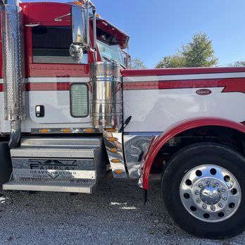Red and silver semi-truck parked on gravel, side view with shiny chrome wheels and steps.