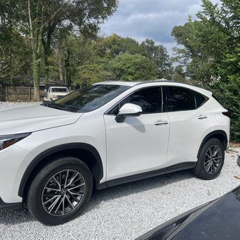 White SUV parked on a gravel roadside with trees and cloudy sky in the background