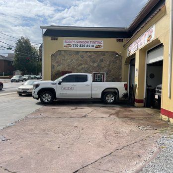 White pickup truck parked outside a metalworking shop with a stone facade and open garage bay