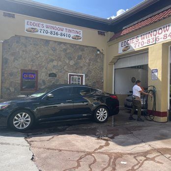 Black sedan at Eddie’s Window Tinting storefront, with a worker using equipment by the open bay.