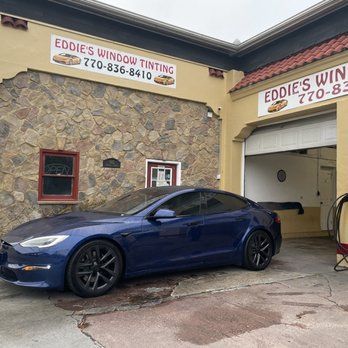 Blue Tesla parked outside Eddie’s Window Tinting shop beside an open garage door.