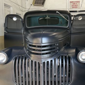 Front view of a matte black vintage truck with chrome grille and open doors in a garage