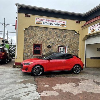 Red sports car parked outside Eddie’s Window Tinting shop with a stone facade.