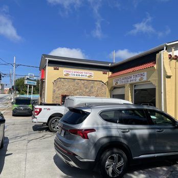 Parking lot outside a yellow storefront with several parked cars under a blue sky.