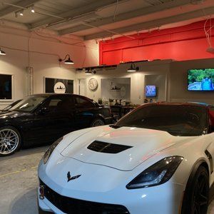 White sports car and black sedan parked inside a garage with red overhead lighting