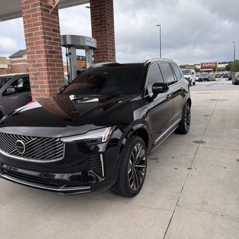 Black Volvo SUV parked at a gas station under cloudy skies