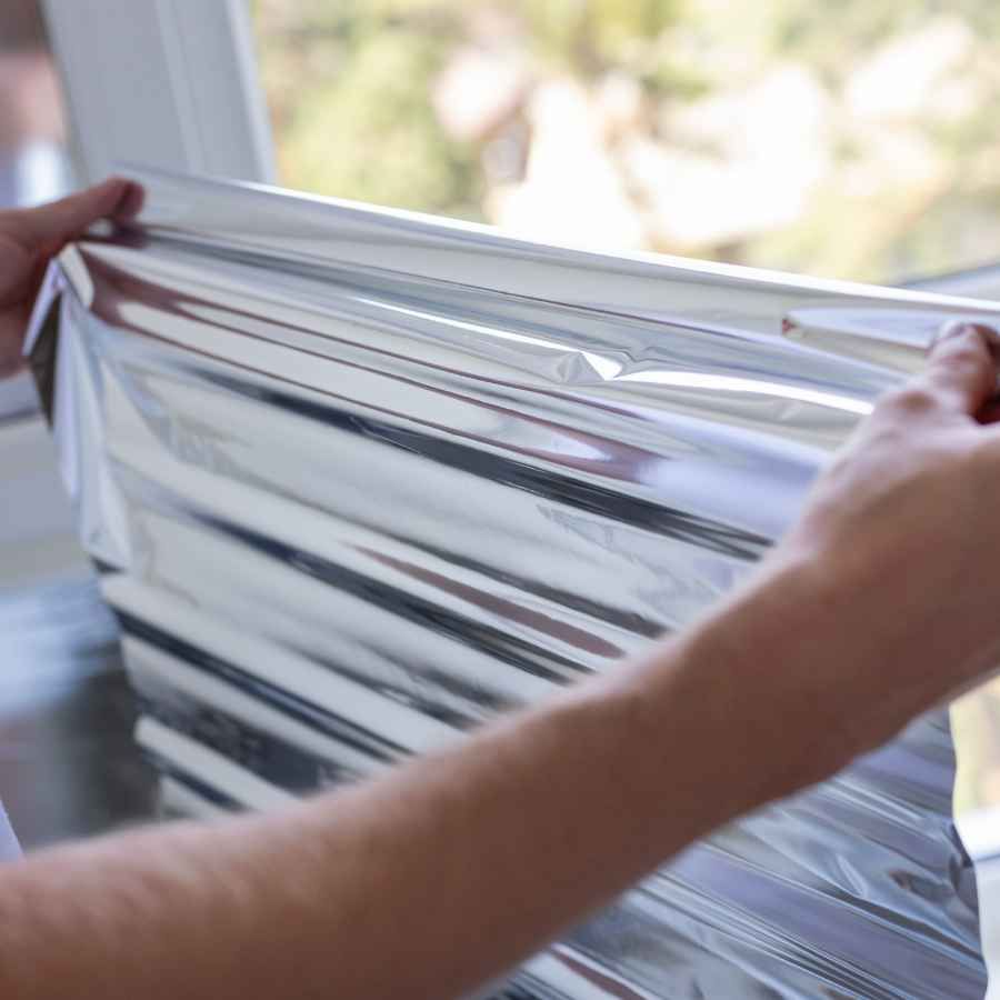 Hands stretching translucent window film across a bright window frame