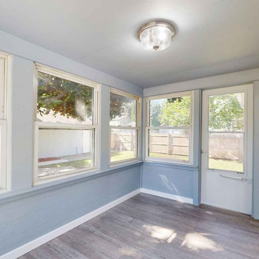 Empty sunroom with light blue walls, gray floor, windows, and a white door overlooking a fenced yard