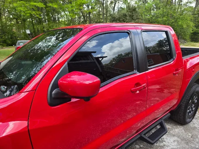 Red pickup truck parked outdoors beside trees, seen from the side.