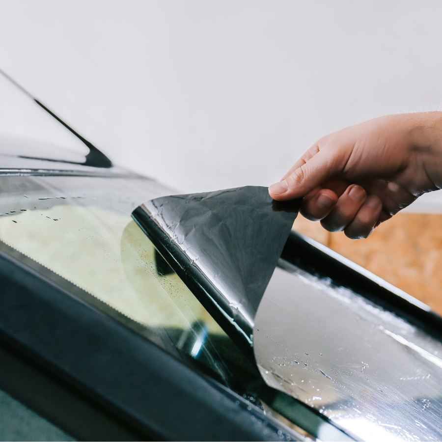 Hand lifting a car window tint film from a windshield corner