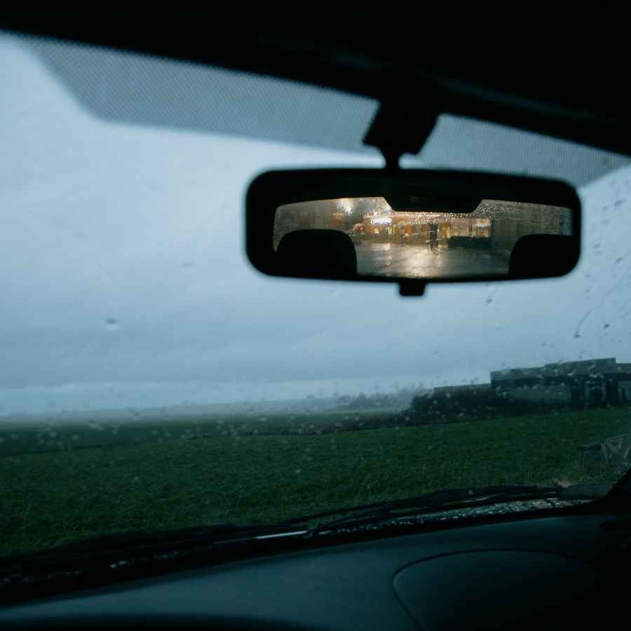 View from inside a car through a rain-speckled windshield toward a cloudy green field at dusk