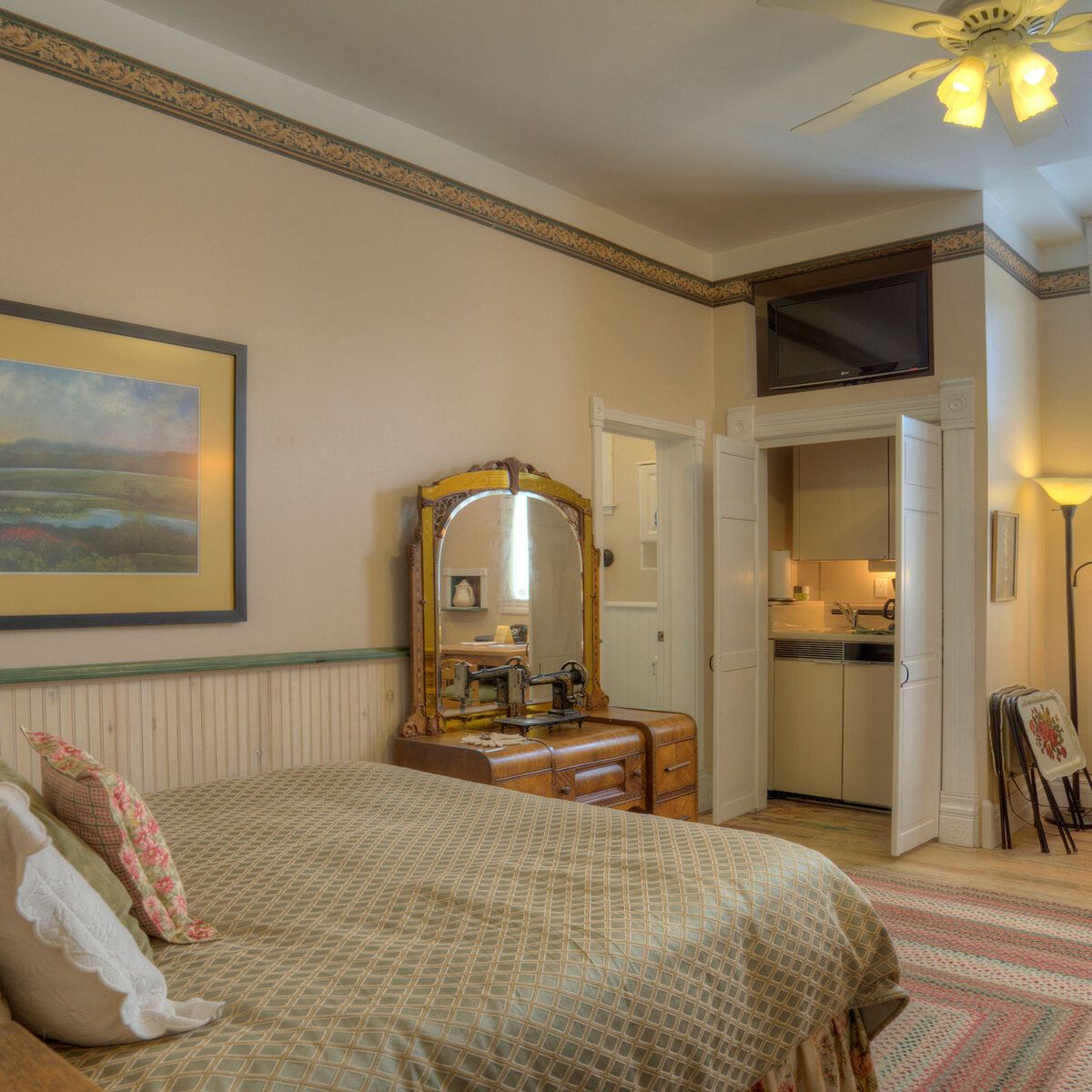 A wide view of a guest room with a bed, dresser, mirror, TV, and kitchenette.