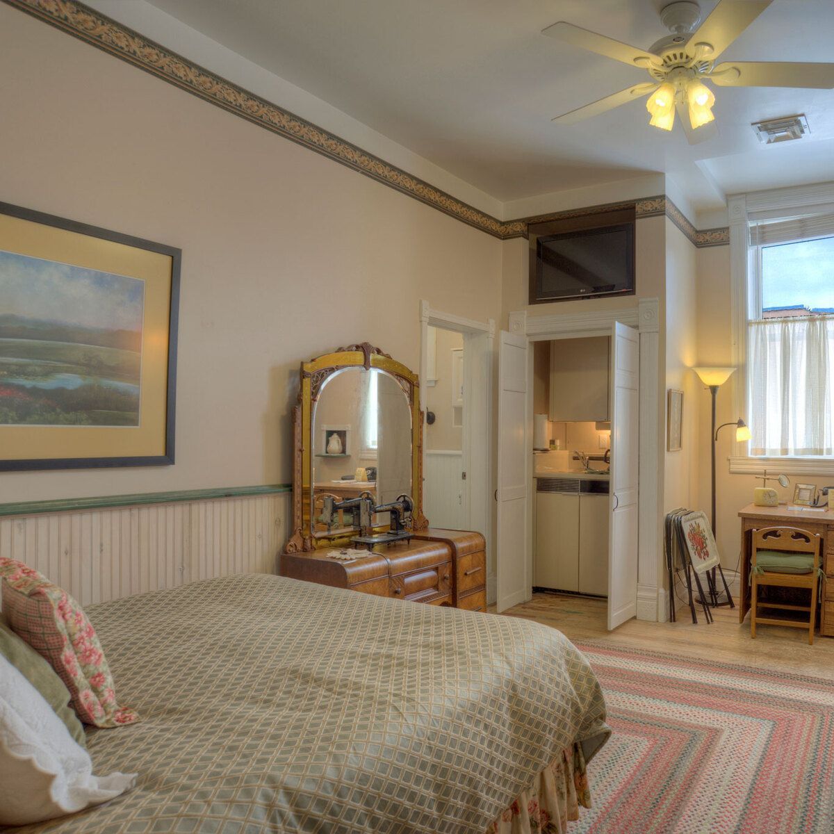 A wide view of a cozy guest room with a bed, dresser, TV, and kitchenette.