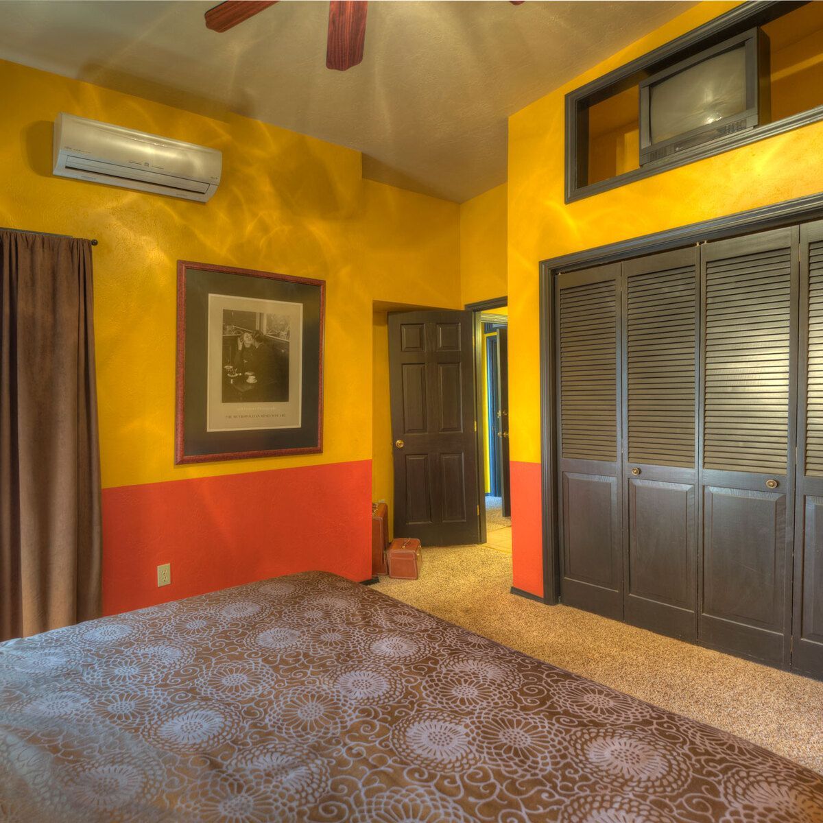 A brightly lit hotel room with yellow and orange walls, a brown door, and a large bed.