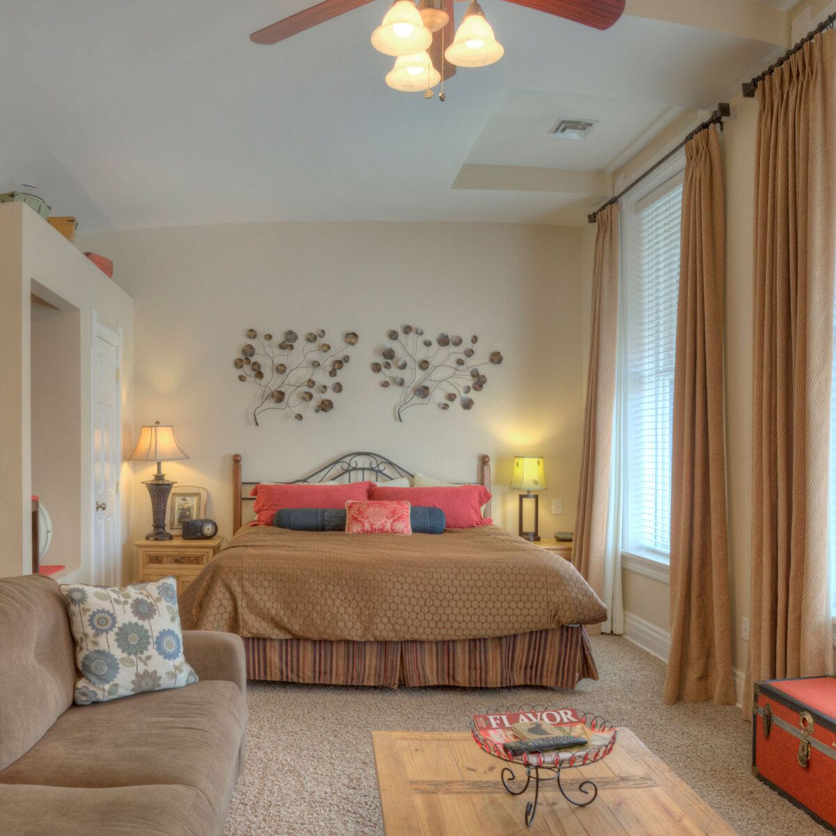 A wide view of a guest room with a bed, sofa, coffee table, and window.