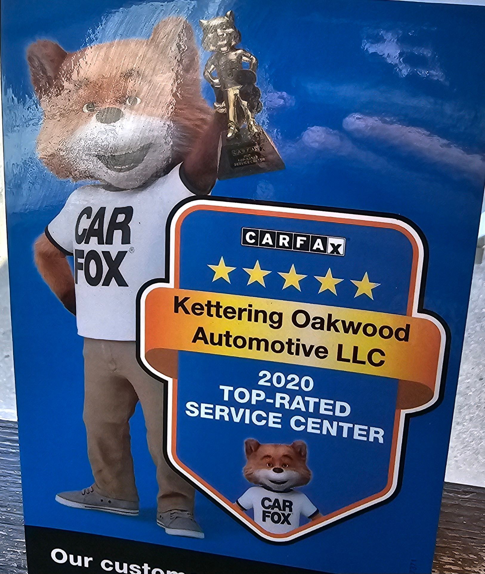 Sign for Kettering Oakwood Automotive. Car Fox mascot holds a trophy. Carfax top-rated service center.