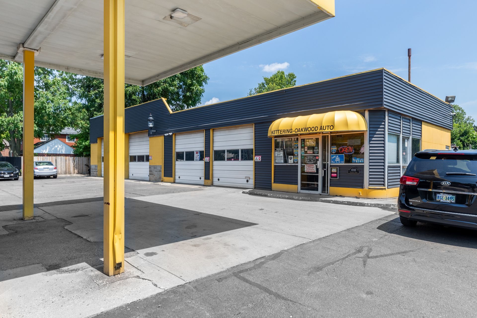 Yellow and black auto repair shop with garage doors, a canopy, and a parked car.