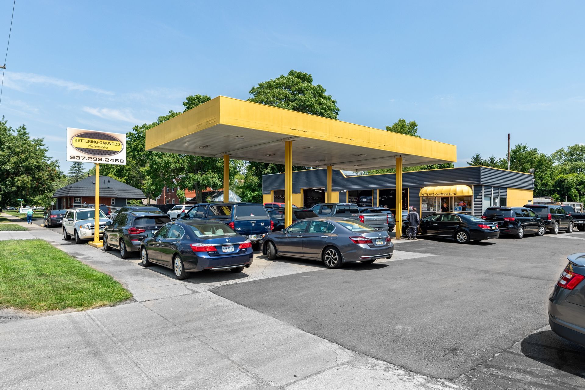 Cars waiting in line at a car wash under a yellow canopy.