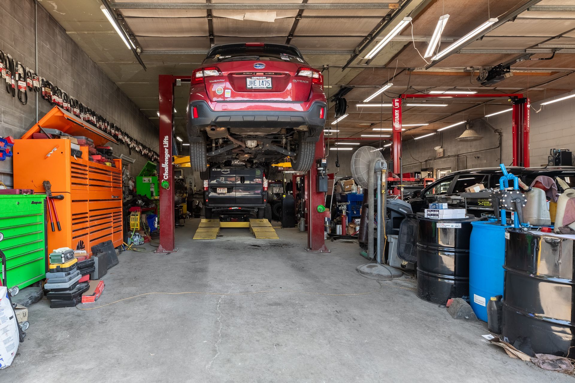 Car on a lift in a cluttered auto repair shop, various tools and supplies visible.