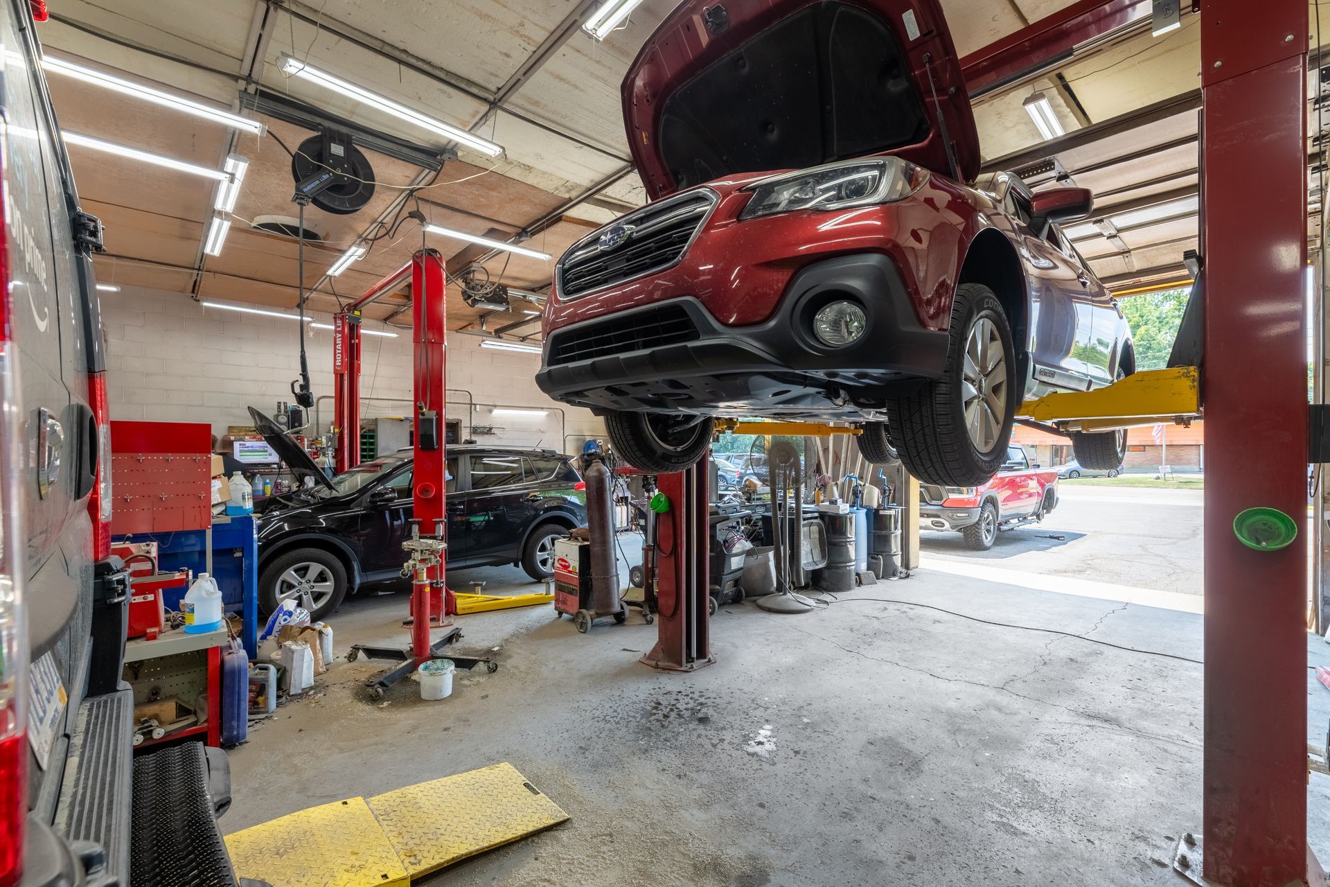 Car repair shop with a red SUV on a lift. Another car is parked nearby.