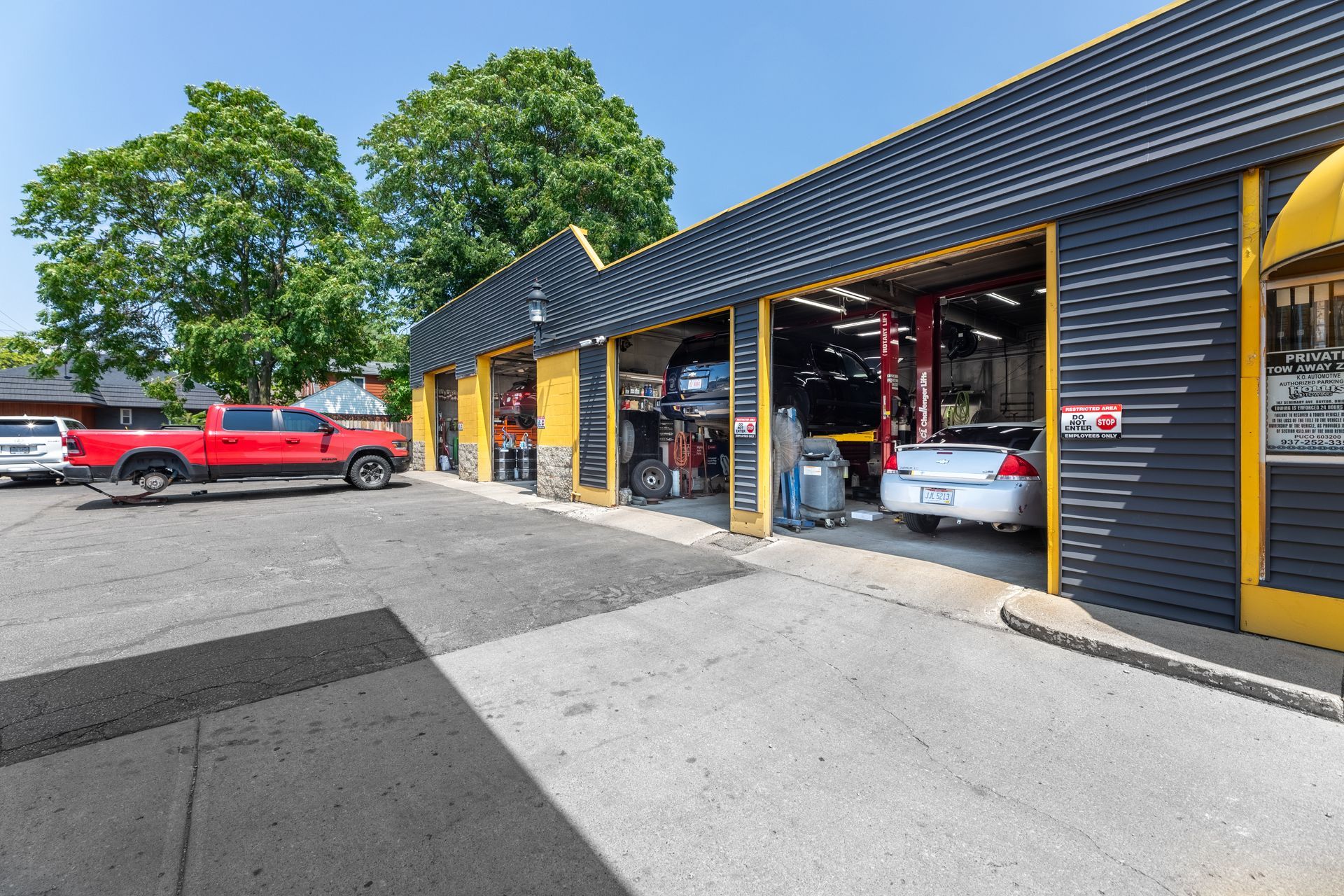 Exterior of a car repair shop with open bays; a red truck and white car are parked outside, one car is lifted.