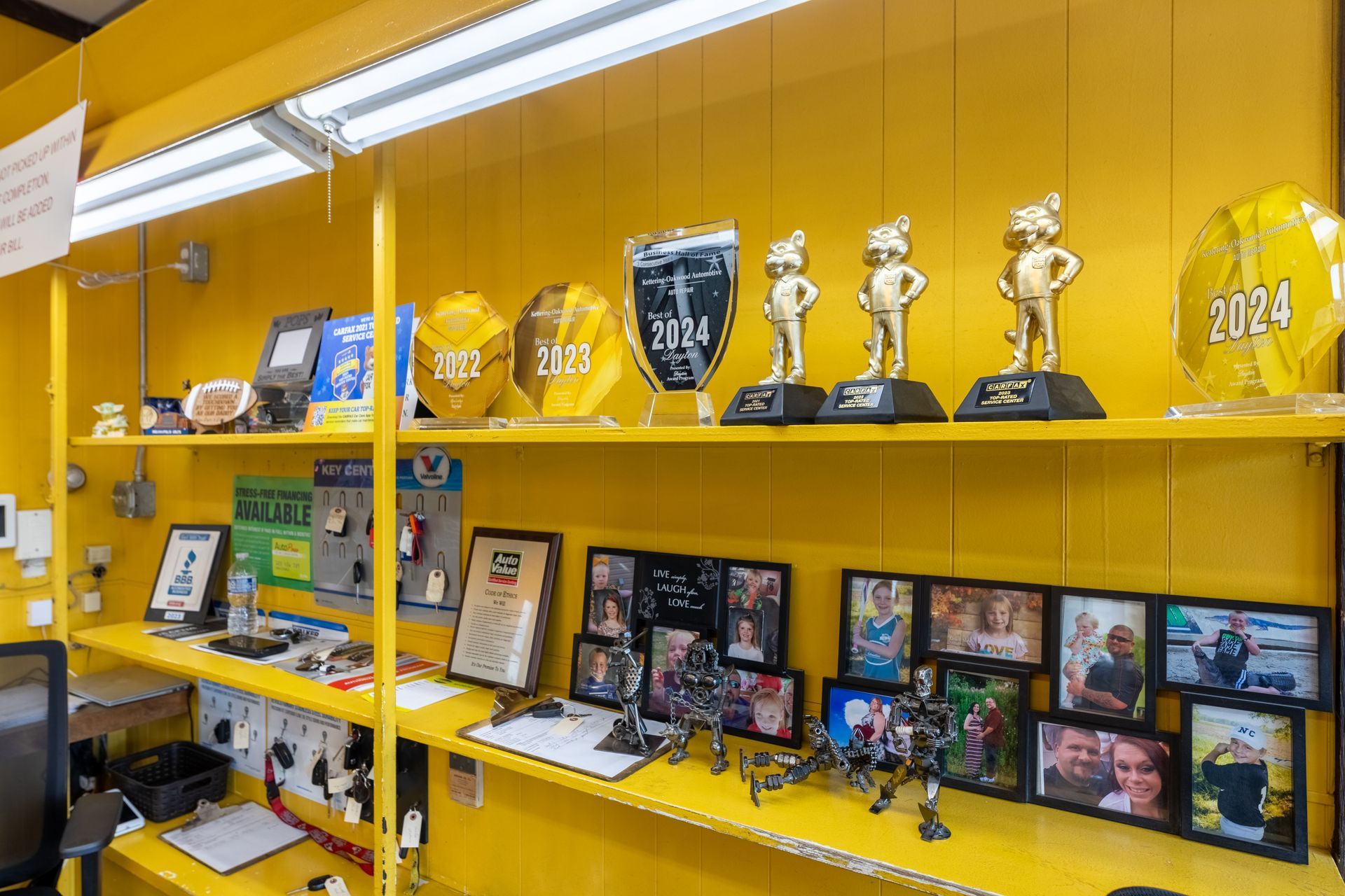 Yellow shelving displays trophies, photos, and small objects against a bright yellow wall.