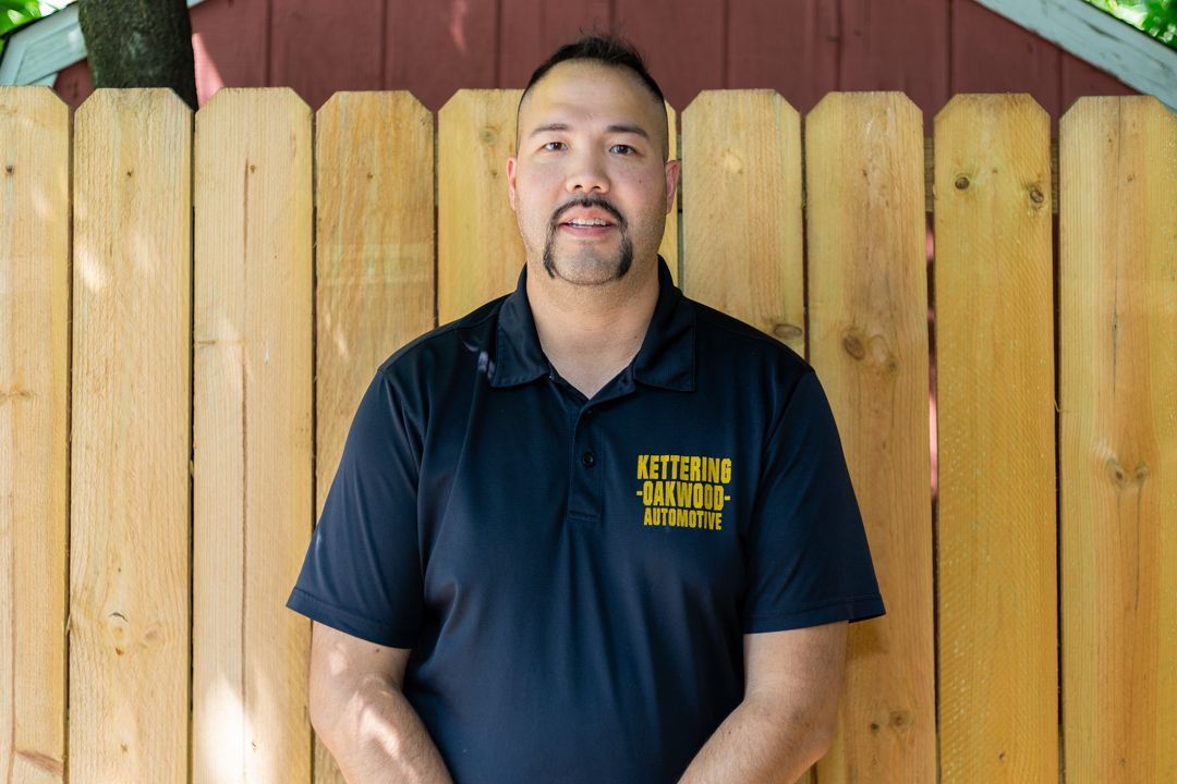 Man in black shirt with logo stands in front of a wooden fence.