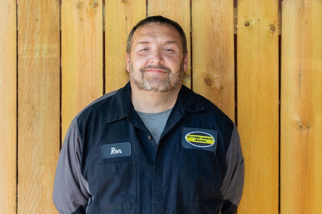 Man in work uniform smiles against a wooden wall.