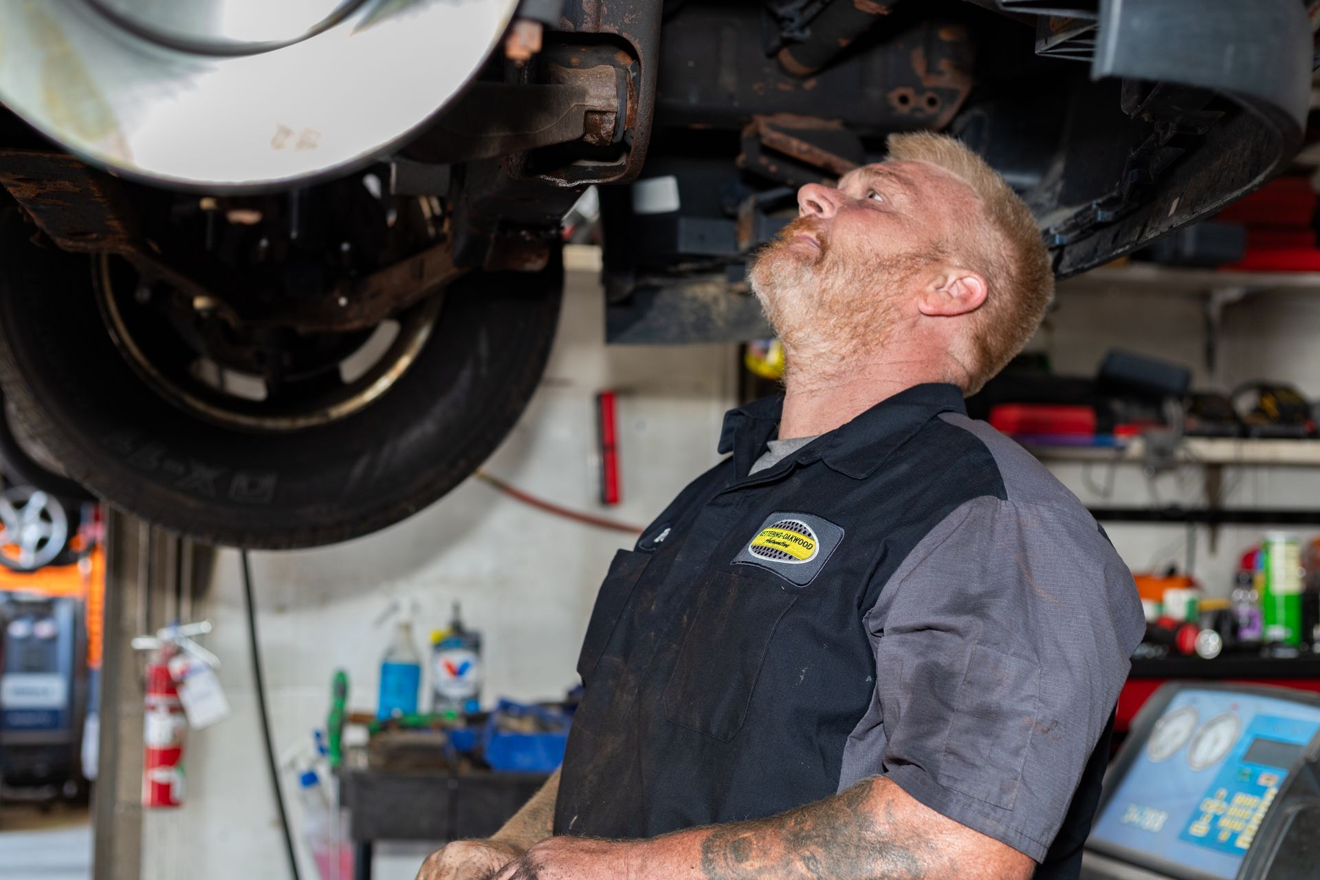 Mechanic inspecting car brakes underneath, looking up; garage setting.