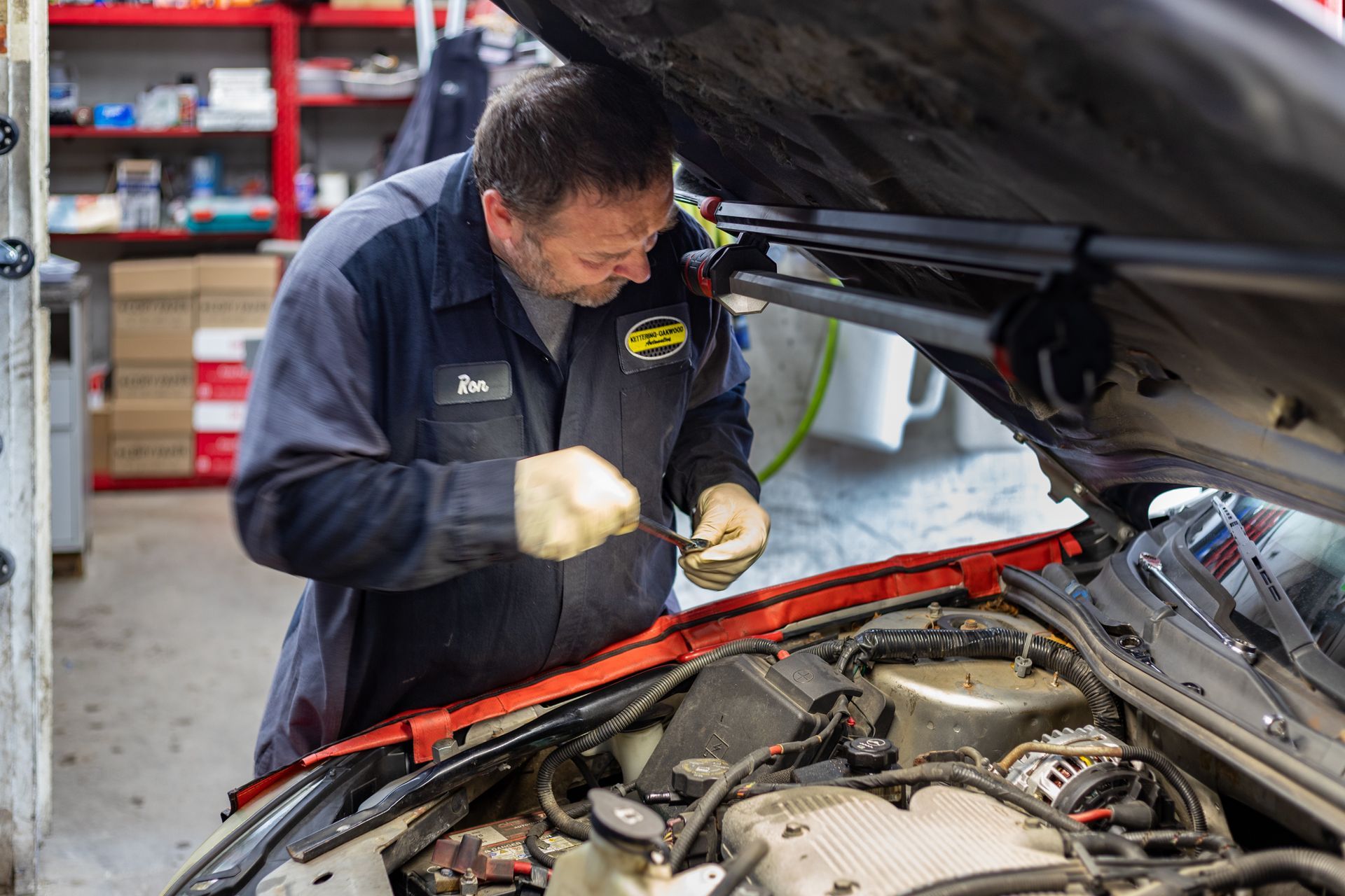 Mechanic in blue jumpsuit works on car engine in a repair shop.