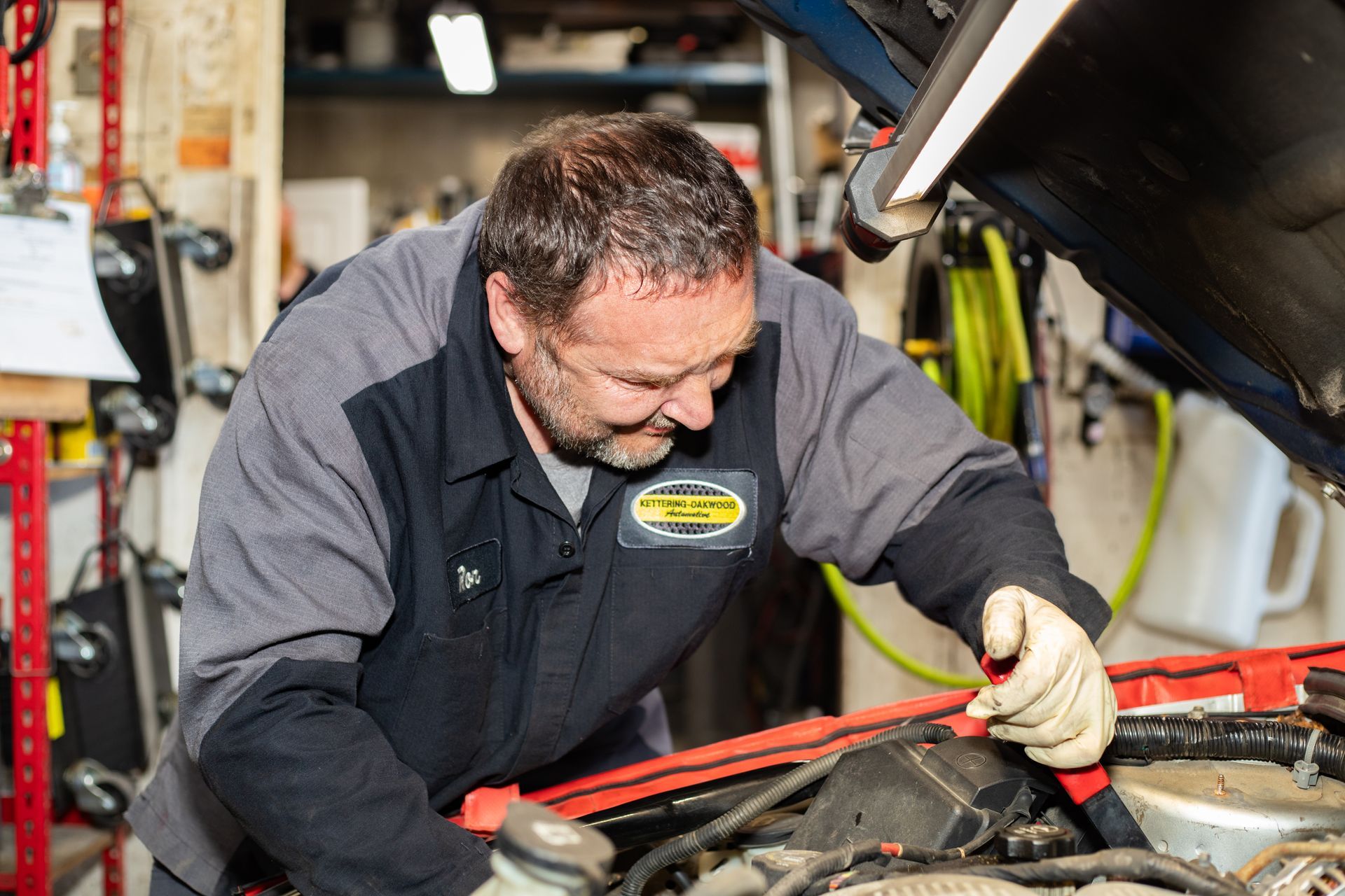Mechanic working on a car engine with the hood open in a garage.