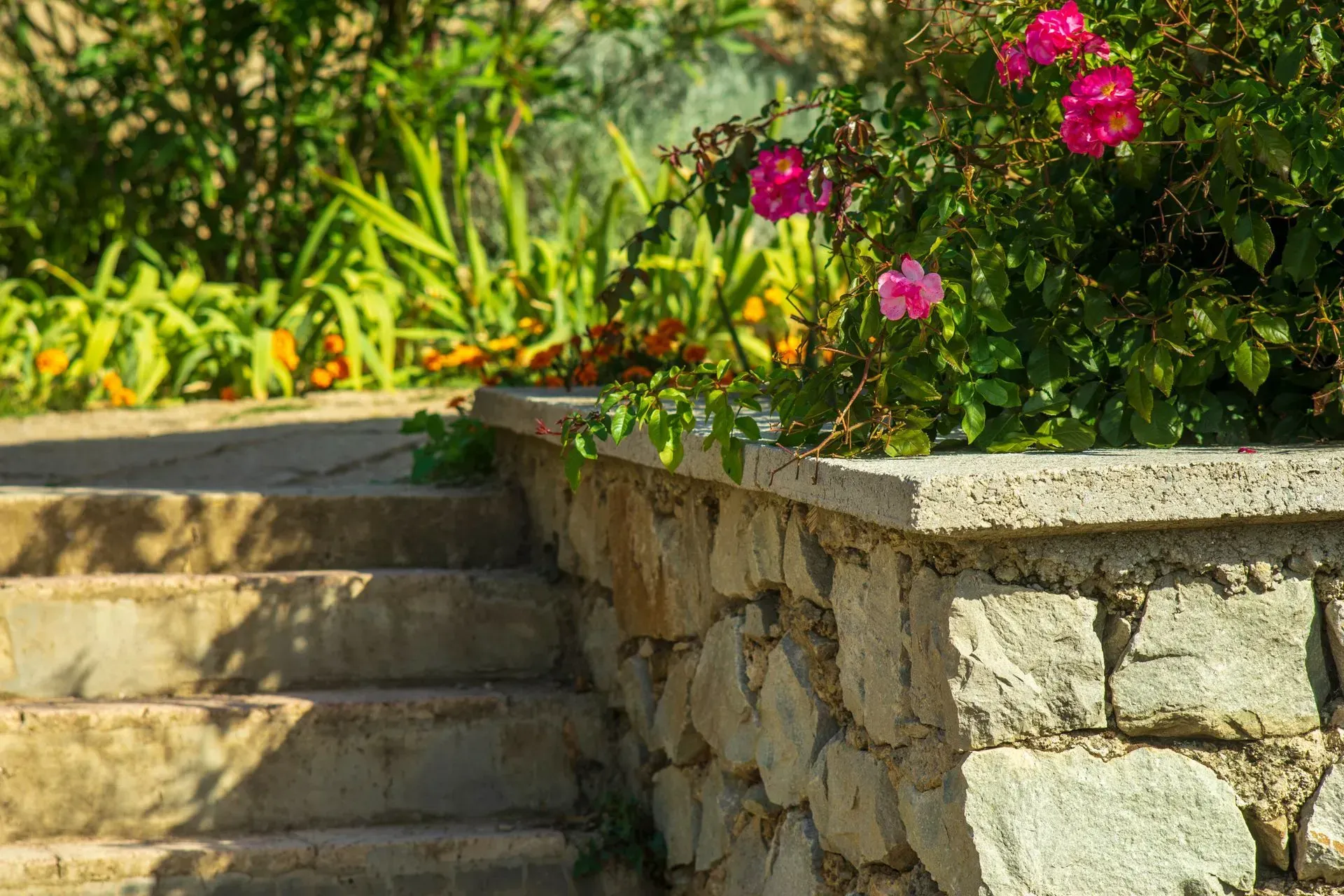 A stone wall with stairs and flowers in the background.