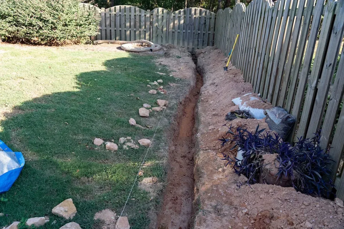 A hole in the ground in a backyard next to a wooden fence.