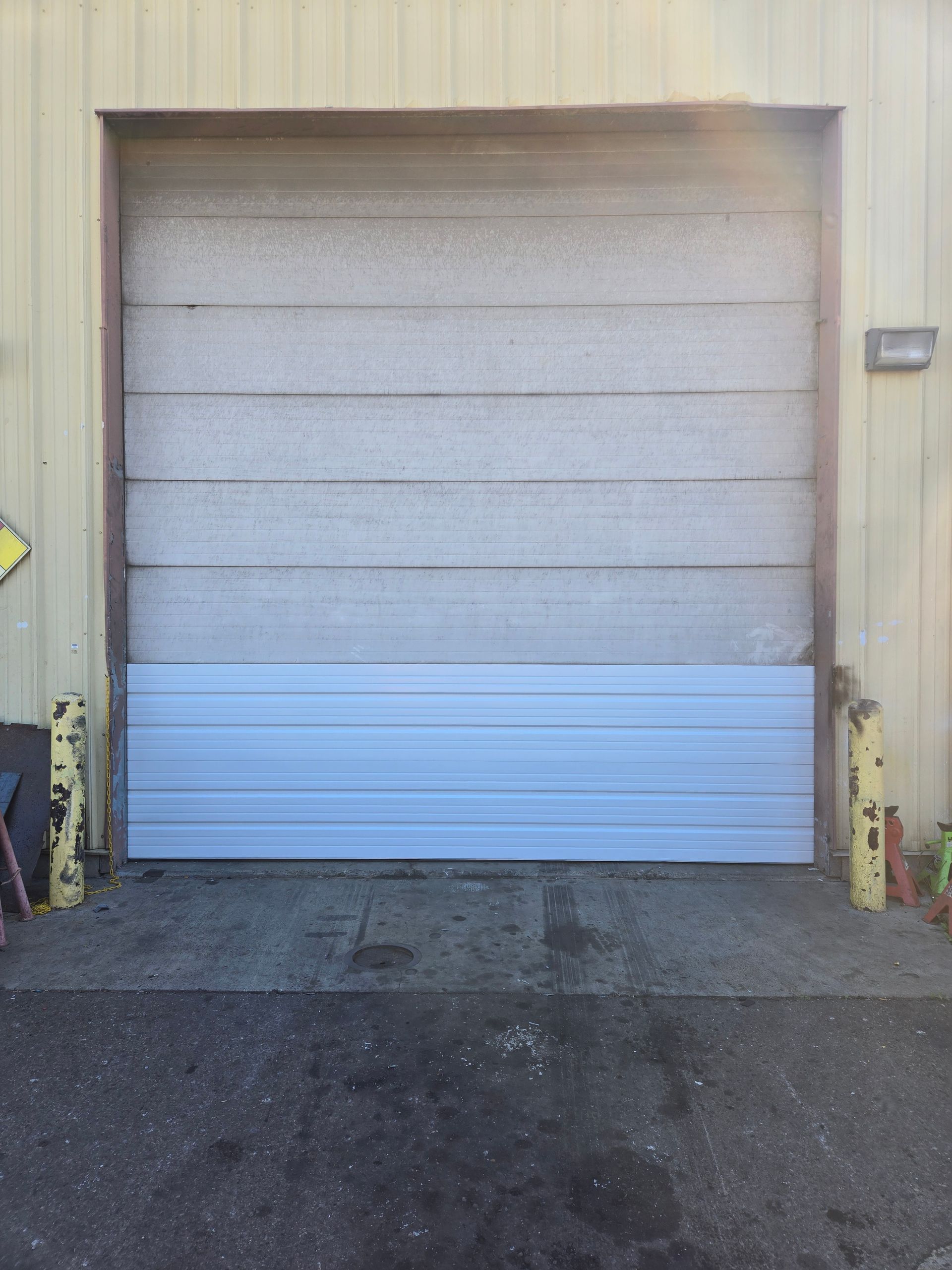 Closed beige roll-up garage door with a blue panel at the bottom on an industrial building