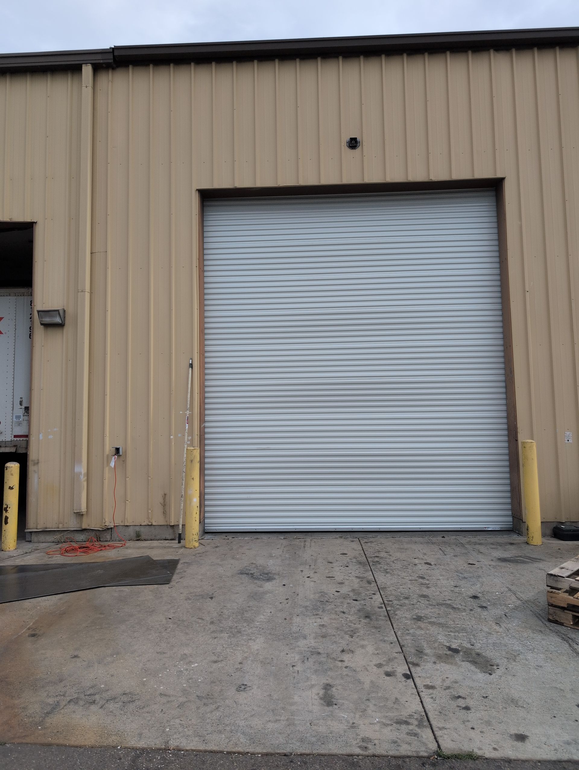 Industrial building with a closed silver roll-up garage door and yellow bollards at the entrance