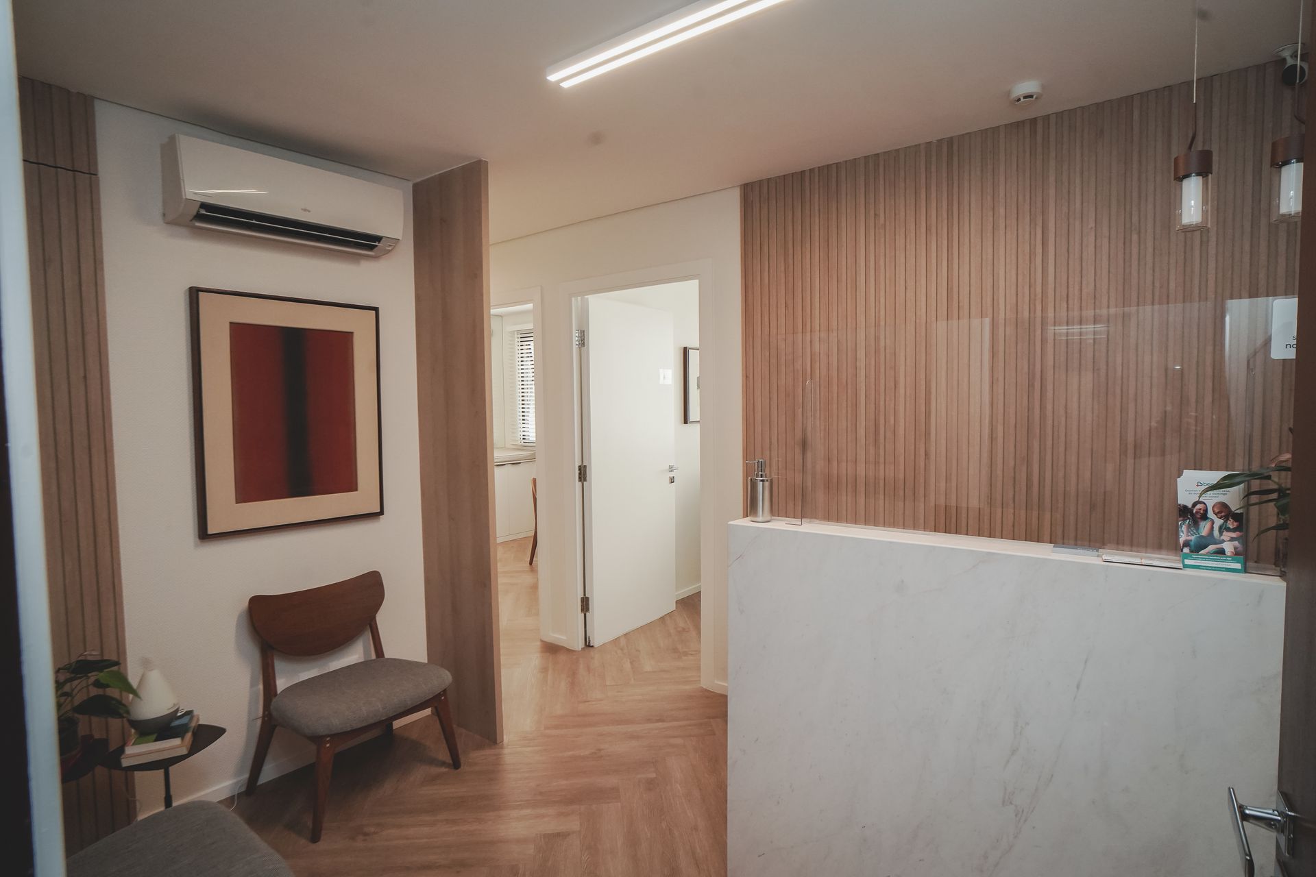 Área de recepção de consultório moderna com paredes revestidas de madeira, balcão branco