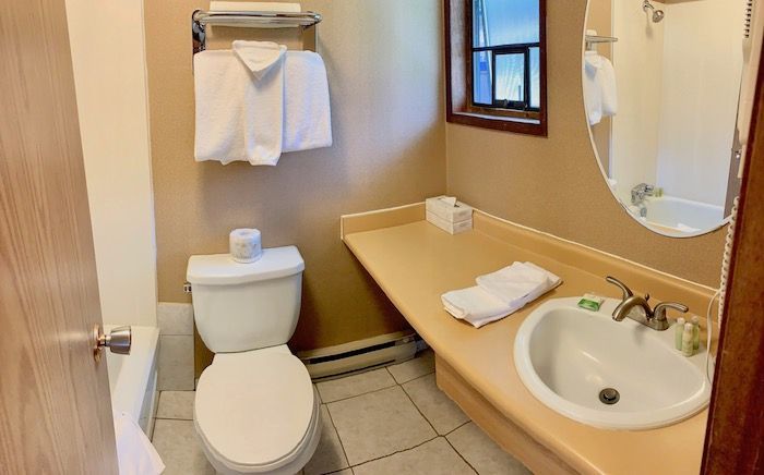 Bathroom with a white toilet, sink, and towels. Tan walls, small window, and light fixtures.