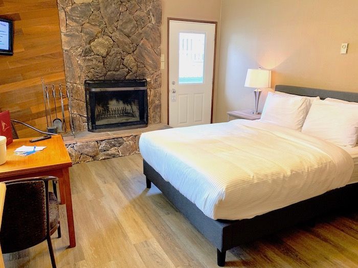 Cozy hotel room with stone fireplace, bed, small table, and a door to the outside.