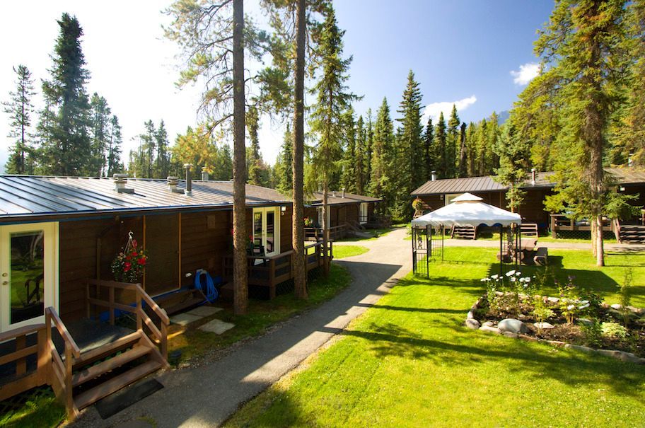 Cabins in a wooded area with a walkway, gazebo, and green lawn on a sunny day.