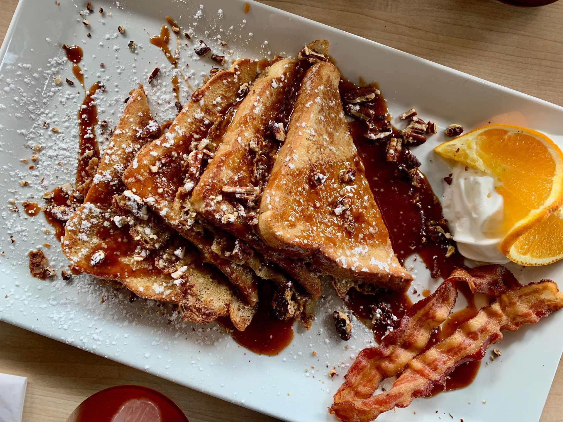 French toast with syrup, nuts, and bacon, garnished with orange slices and whipped cream.